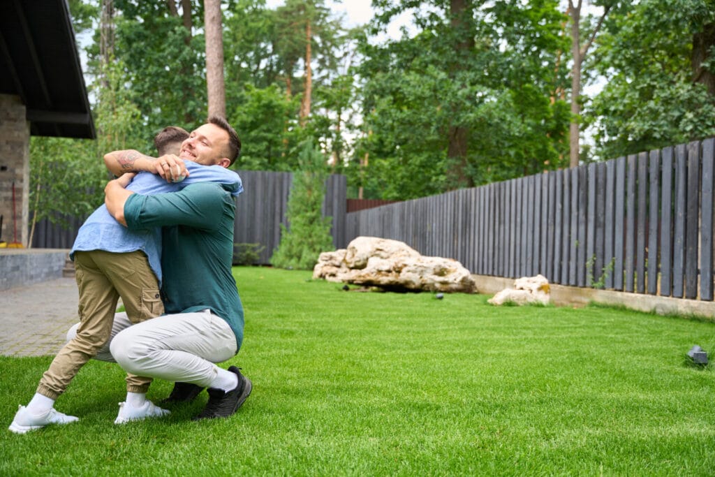 smiling father hugs his son on the lawn of house